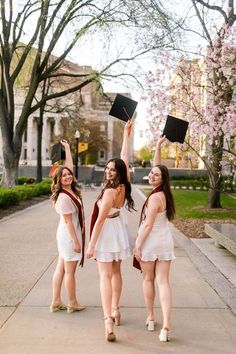 three girls in graduation gowns throwing their hats into the air while standing on a sidewalk