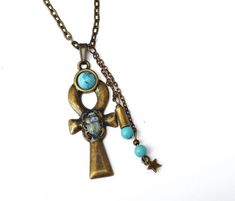 "A mystical necklace featuring a large Egyptian ankh pendant with a scarab beetle decoration, an ancient symbol of the resurrection of life, accented with painted touches of lustrous violet and turquoise! A little violet quality \"S\" crystal rhinestone sparkles from its back and turquoise blue magnesite beads dangle alongside the unique pendant! A faux turquoise stone sits at the top of the ankh pendant as yet another design element. The luck-bringing pendant dangles from a sturdy antiqued gold Bohemian Ankh-shaped Bronze Jewelry, Bohemian Ankh Shaped Jewelry For Festivals, Bohemian Ankh Bronze Jewelry, Bronze Ankh Bohemian Jewelry, Bohemian Ankh Jewelry For Festivals, Bronze Cross Bohemian Necklace, Bronze Bohemian Cross Necklace, Bohemian Bronze Cross Necklace, Bohemian Ankh Necklace For Festivals