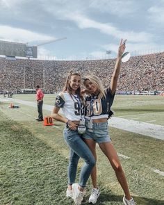 two girls standing on the sidelines at a football game, one holding her arm up in the air