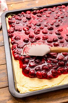 a pan filled with cake covered in cherries and topped with a wooden spatula