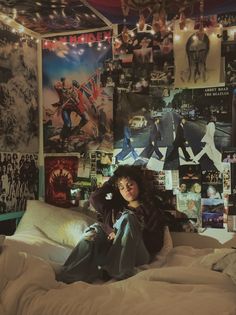 a woman sitting on top of a bed covered in posters and lights above her head