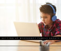 a young boy sitting at a table with headphones on and looking at a laptop