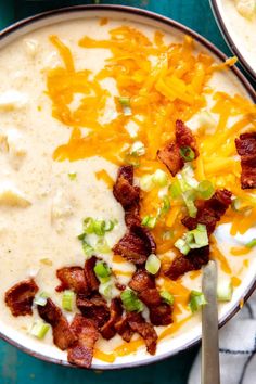 two bowls of potato soup with bacon, cheese and green onions on the side next to a spoon