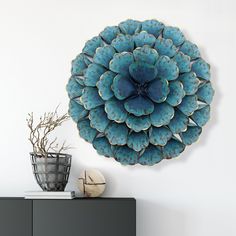 a large blue flower is hanging on the wall next to a vase with flowers in it