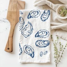 a white dish towel with blue shells on it next to a wooden spoon and bowl