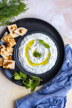 a black plate topped with pita bread and white sauce next to green garnish