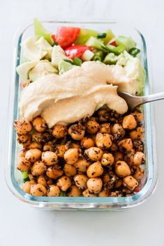 a salad in a glass dish with dressing on the side, including lettuce and chickpeas