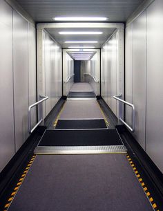 an empty hallway with metal railings leading up to the exit door on either side