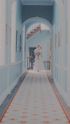 a woman in a white dress is walking down a hallway with red and white tiles on the floor