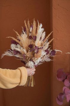 a woman holding a bouquet of dried flowers in her hand with purple and white petals