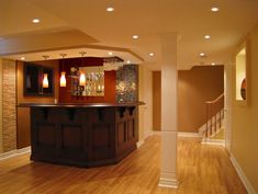 an empty living room with hard wood flooring and lights on the ceiling, along with a bar