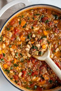 a pot filled with beans and vegetables on top of a white table cloth next to a wooden spoon