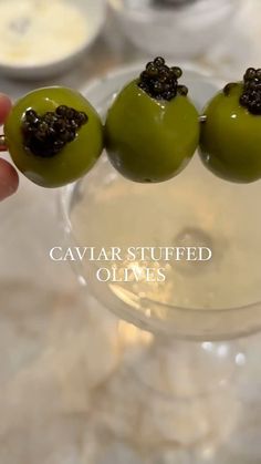 three green olives in a wine glass with black caviar stuff on top