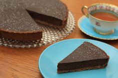 a piece of chocolate cake on a blue plate next to a cup of tea and saucer