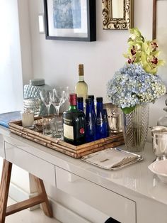 a tray with bottles and glasses on top of a table next to a vase filled with flowers