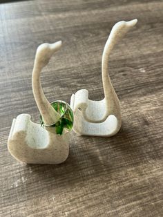 two white ceramic sculptures sitting on top of a wooden table with a green plant in the middle