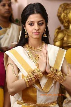 a woman wearing gold jewelry and holding her hands up to her face while standing in front of a mirror