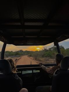 two people sitting in the back of a truck on a dirt road as the sun sets