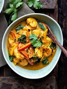 a bowl filled with shrimp and vegetables on top of a wooden table next to a spoon