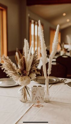 there are two vases with feathers in them on the table at this wedding reception