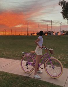 a woman is standing next to her bike on the side walk at sunset or dawn