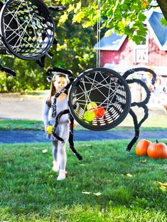 a spider mobile hanging from a tree in the grass with two girls walking behind it