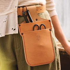 a person holding a brown leather case with scissors and other items in it's pocket