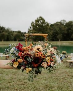 a woman holding a bouquet of flowers in her hand at an outdoor wedding ceremony by the water