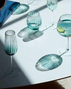 several wine glasses are lined up on a table with shadows from the sun shining through them