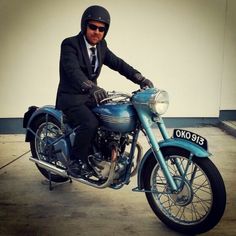 a man in a suit and tie sitting on a blue motorcycle with his helmet on