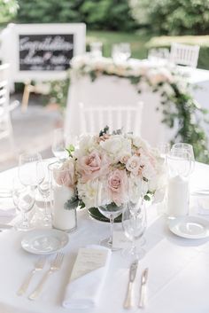 the table is set with white and pink flowers, silverware, candles and napkins