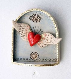 a ceramic heart with wings and an eye on the top is hanging from a wall