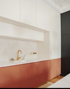 a kitchen with red cabinets and white counter tops, gold faucet in the middle