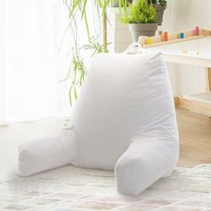 a large white pillow sitting on top of a floor next to a potted plant