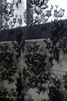 black and white photograph of sheer curtains with floral laces on the window sill