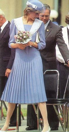 a woman in a blue dress and hat standing next to other people