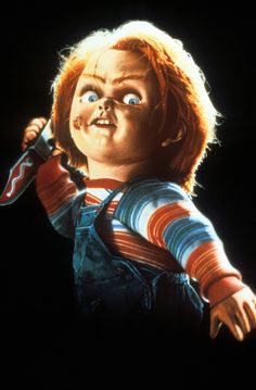 the chucky doll is wearing overalls and holding a large toothbrush in his mouth