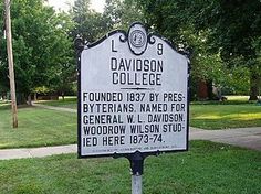 a sign in front of a grassy area with trees and grass on the side walk