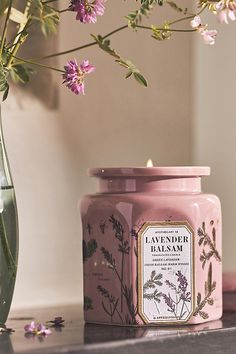 a pink jar sitting on top of a table next to a vase filled with flowers