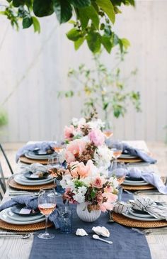 an outdoor table set with plates and place settings, flowers in a vase on the table