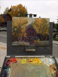 an artist's easel with paint and brushes in front of a house on the street