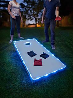 a man and woman standing next to a lighted cornhole game