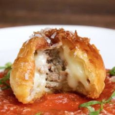 a meatball stuffed with cheese and tomato sauce on a white plate topped with basil leaves