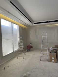 a man is painting the walls in an empty room with ladders and boxes on the floor