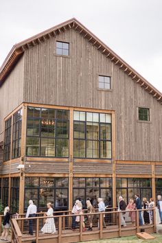 a group of people standing outside of a large wooden building next to a lush green field