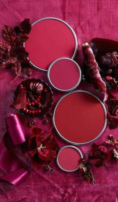 three different shades of red on a pink cloth with flowers and other items around it