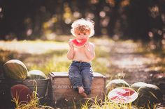 a little boy sitting on top of a wooden crate with watermelon in the background