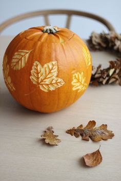 an orange painted pumpkin sitting on top of a table next to leaves and acorns