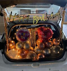 a car trunk filled with lots of shiny balls and helium balloons that say happy birthday