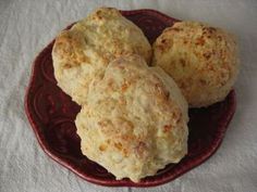 three biscuits sitting on top of a red plate next to a white cloth covered table